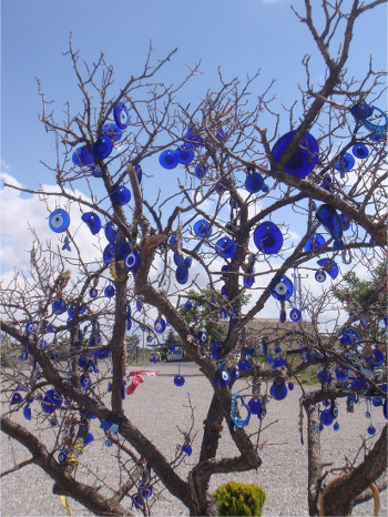 A bare-branched tree with dozens of blue nazar, whole and broken alike